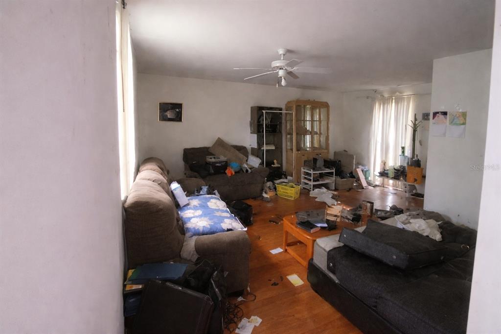 A cluttered living room features wood-look flooring, a ceiling fan, and several pieces of furniture — 7393 GRAND AVENUE, WINTER PARK, FL