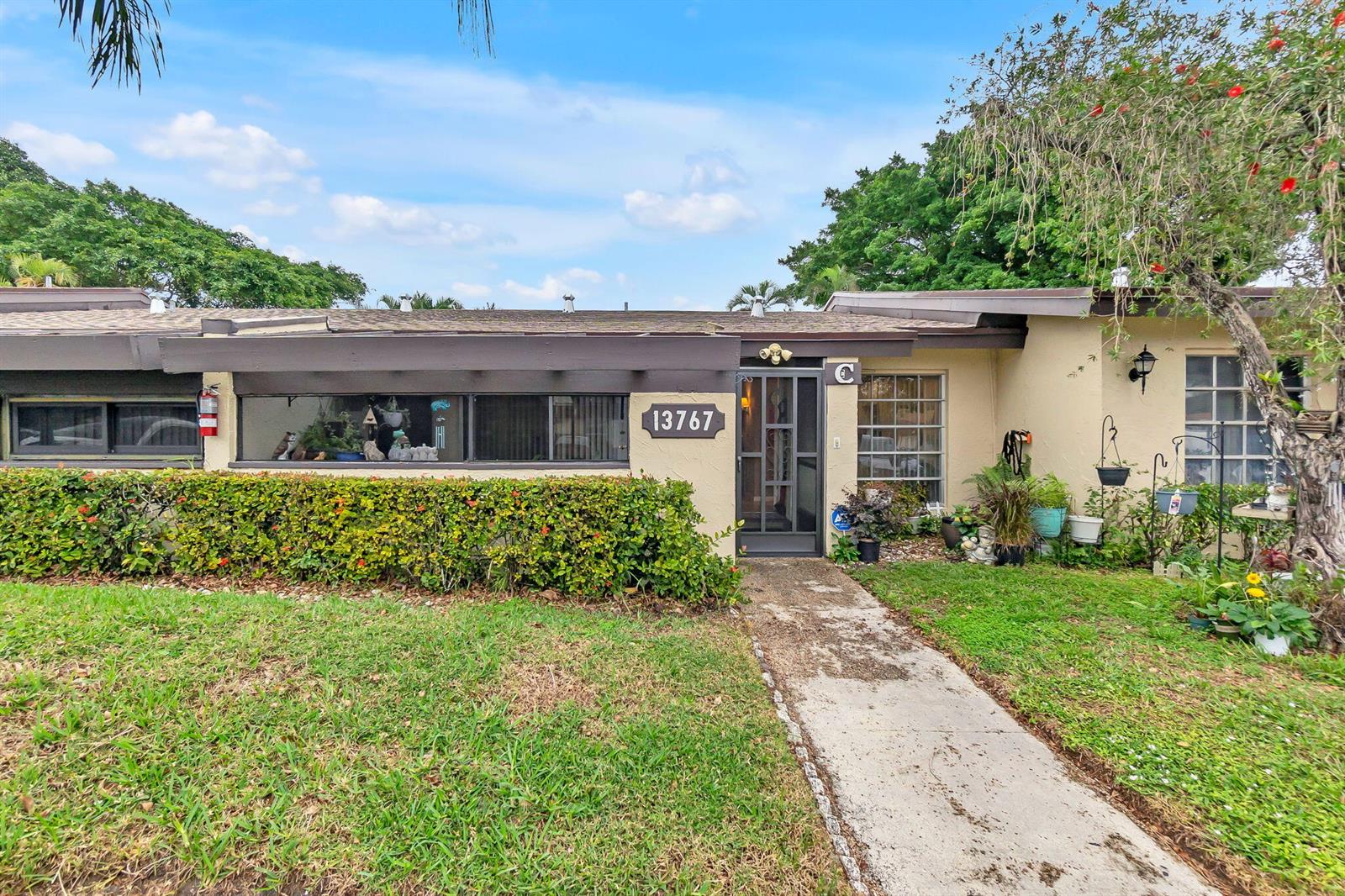 A single-story residential building with a beige stucco exterior, a dark brown roof, and landscaping — 13767 Via Aurora # C, Delray Beach FL 33484, DELRAY BEACH, FL