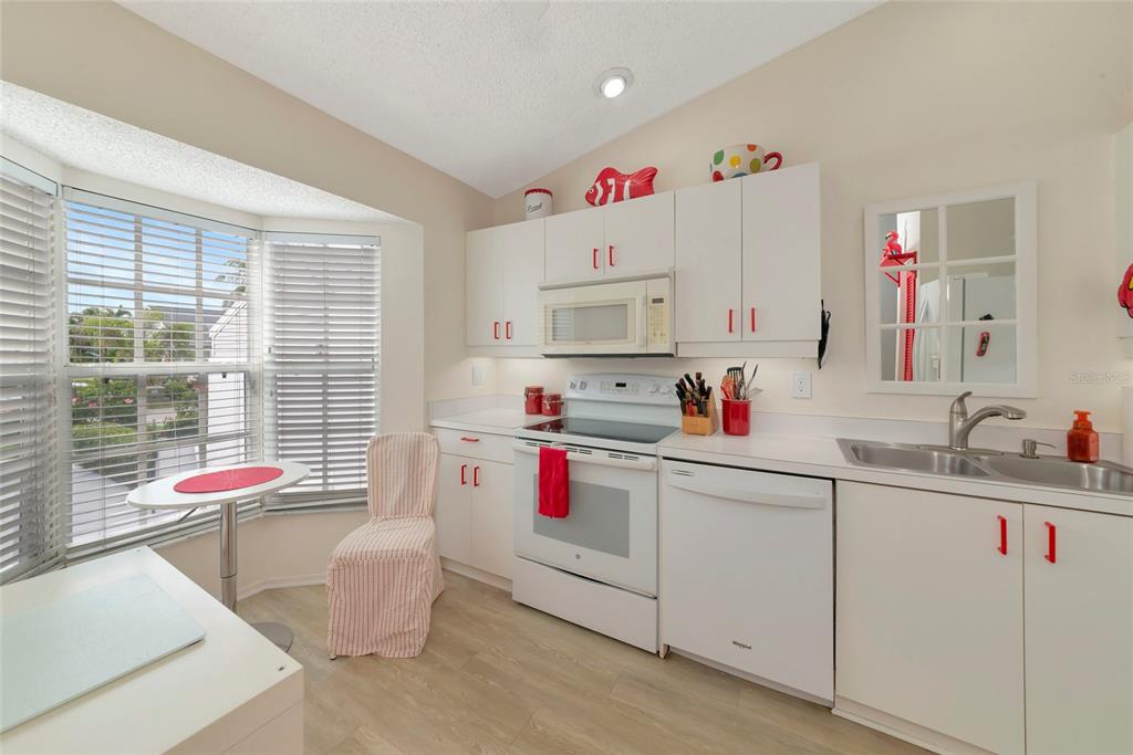 A kitchen features white cabinetry, white appliances, a double sink, and a small dining nook — 1216 SPOONBILL LANDINGS CIRCLE, BRADENTON, FL