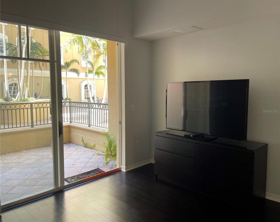 A room with dark wood floors, a television on a dresser, and a sliding glass door — 1064 N TAMIAMI TRAIL UNIT 1122, SARASOTA, FL