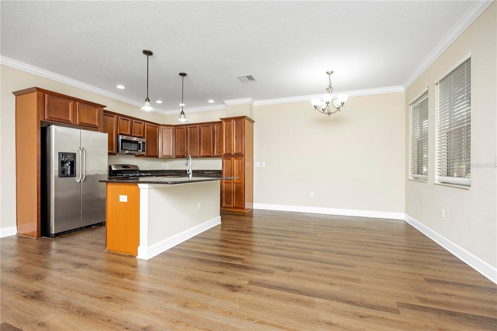 A kitchen with wood cabinets, stainless steel appliances, and an island opens to a dining area — 6112 FISHHAWK CROSSING BOULEVARD, LITHIA, FL