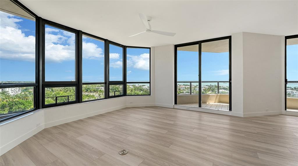 An empty room with light wood flooring, a ceiling fan, and large windows overlooking trees — 1211 GULF OF MEXICO DRIVE UNIT 701, LONGBOAT KEY, FL