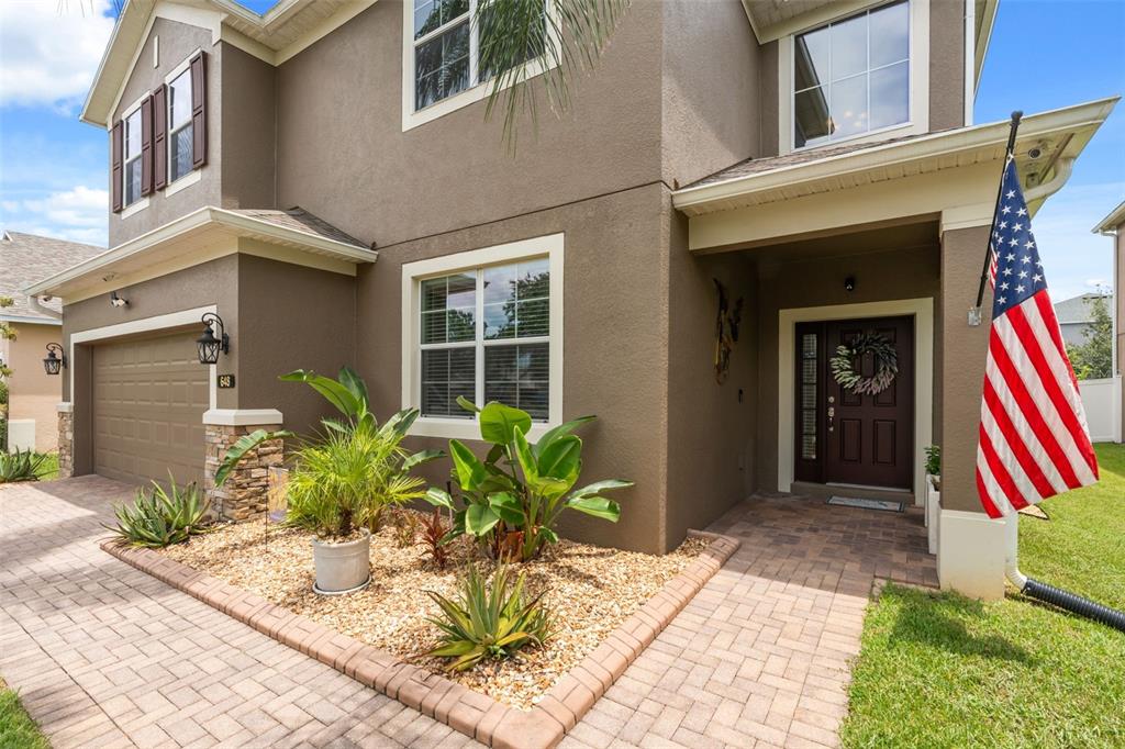 A two-story house exterior with a paved driveway, front garden, and an American flag — 648 CORTONA DRIVE, ORLANDO, FL