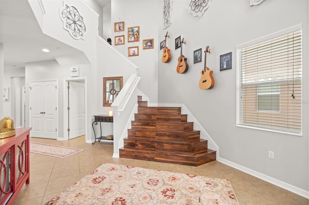 A foyer features a staircase with wood-look steps, a patterned rug, and guitars on the wall — 648 CORTONA DRIVE, ORLANDO, FL