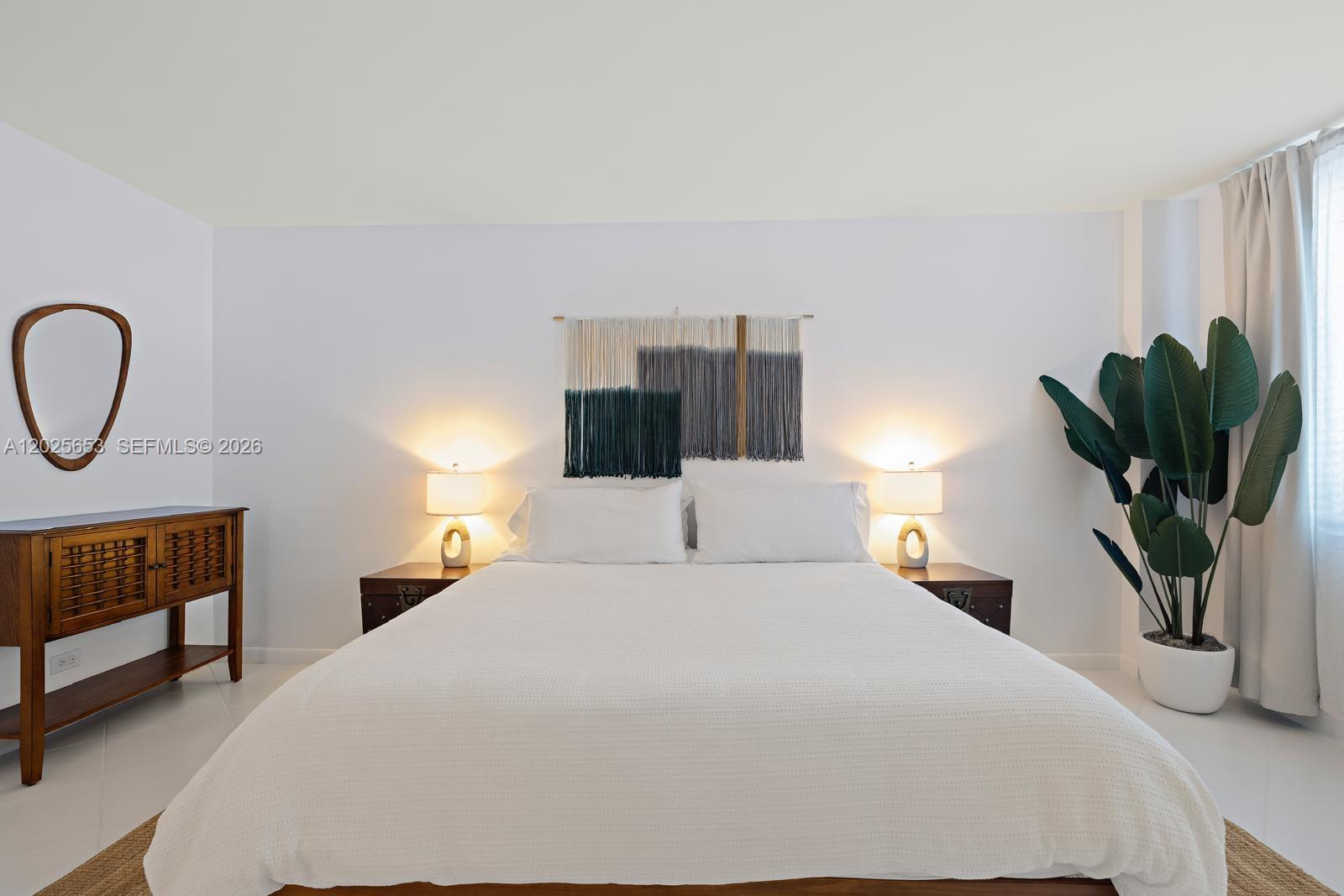 A bedroom features a white bed, two bedside lamps, wall art, and a potted plant — 2301 Collins Ave # 519, Miami Beach FL 33139, MIAMI BEACH, FL