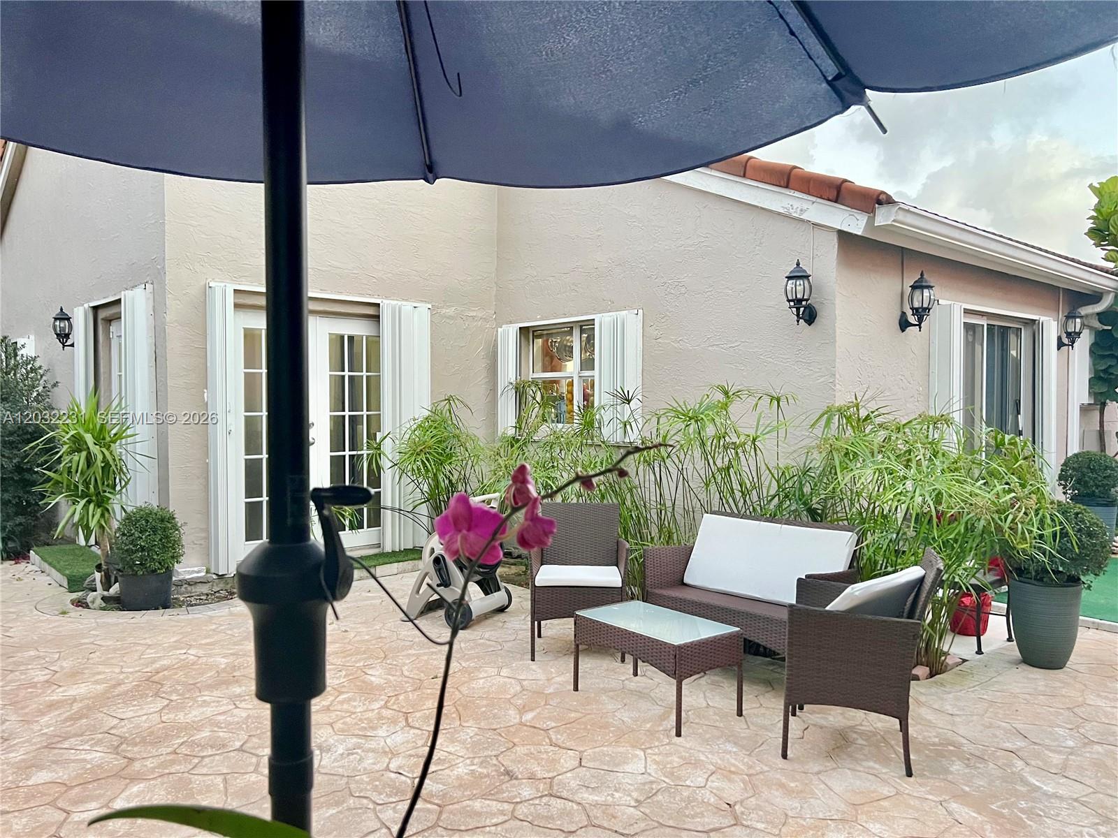 A patio features wicker furniture, a glass-topped table, potted plants, and an umbrella — 11769 SW 92nd Ln, Miami FL 33186, MIAMI, FL