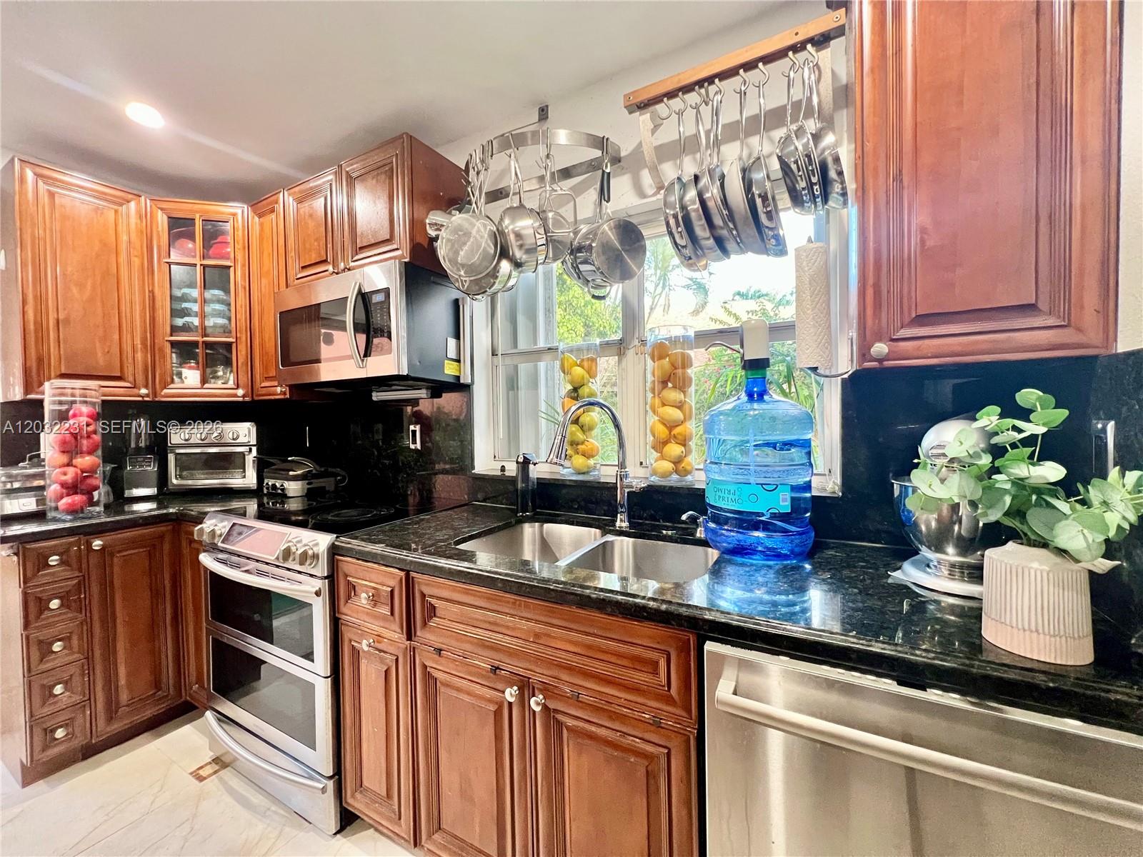 A kitchen features wood cabinets, black granite countertops, stainless steel appliances, and a hanging pot rack — 11769 SW 92nd Ln, Miami FL 33186, MIAMI, FL
