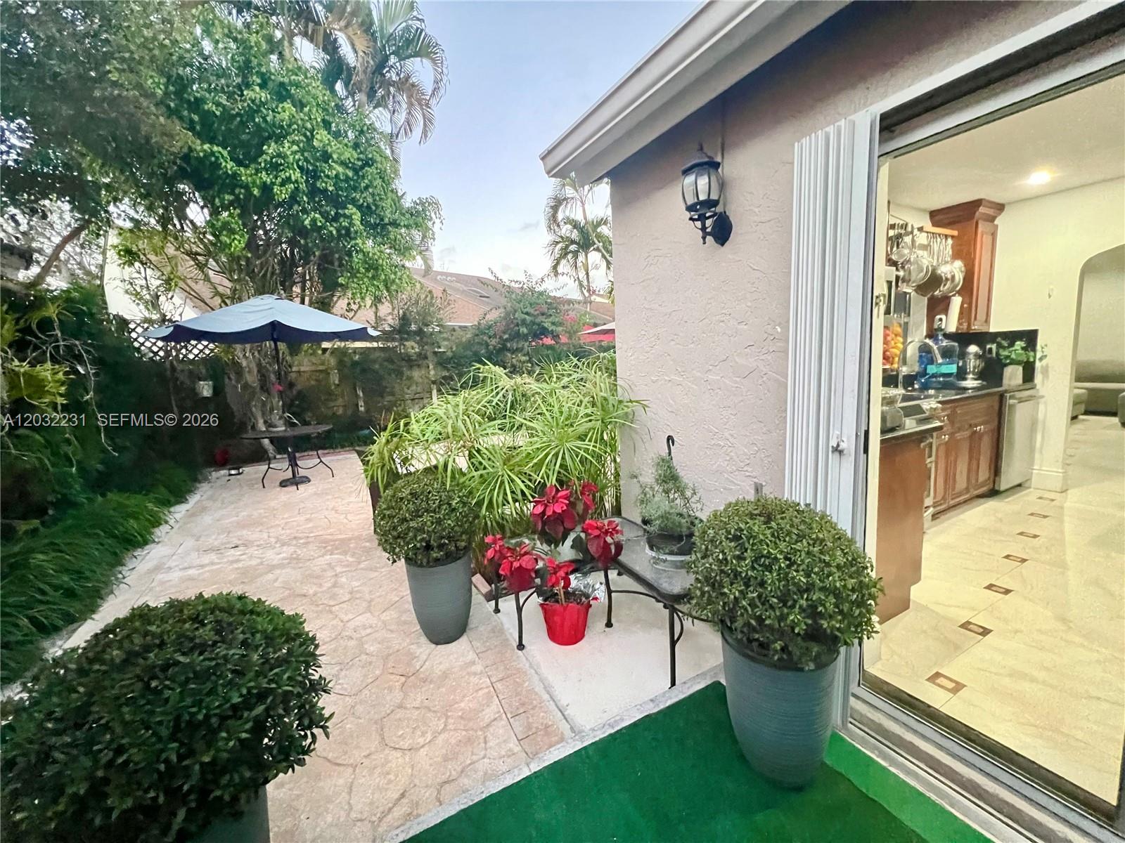 A patio with potted plants and a table sits outside a house with a kitchen — 11769 SW 92nd Ln, Miami FL 33186, MIAMI, FL