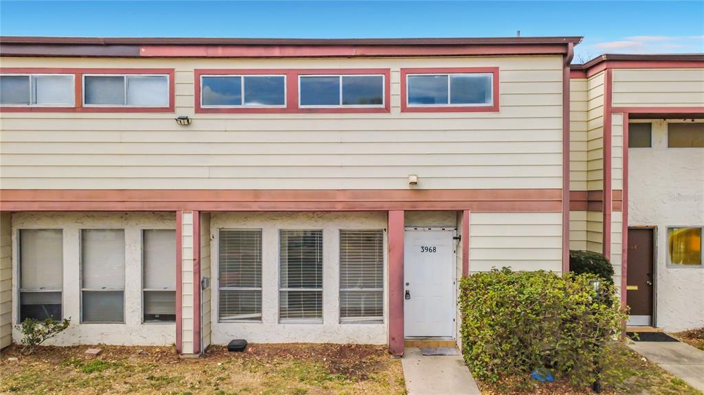 A two-story townhouse exterior features beige horizontal siding, red trim, and a white front door — 3968 CRAYRICH CIRCLE UNIT C3, ORLANDO, FL