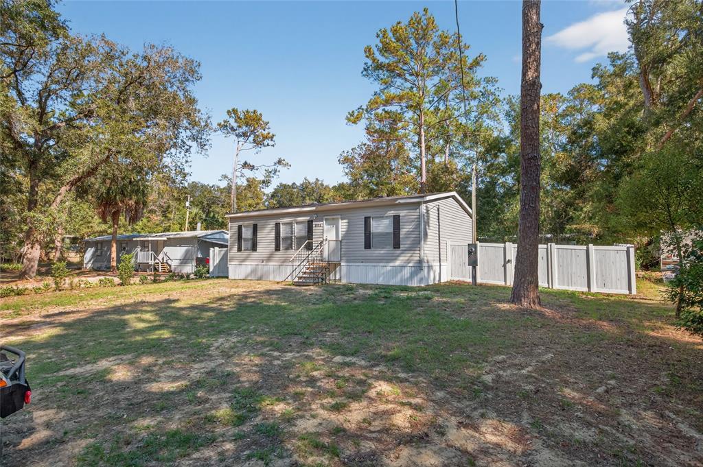 A gray manufactured home sits on a grassy lot with a white privacy fence — 3883 SE 55TH COURT, OCALA, FL