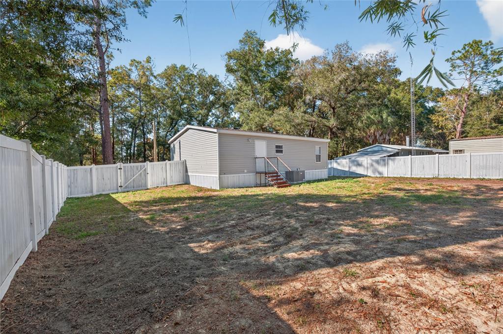 A gray manufactured home sits in a fenced backyard with sparse grass and sandy soil — 3883 SE 55TH COURT, OCALA, FL
