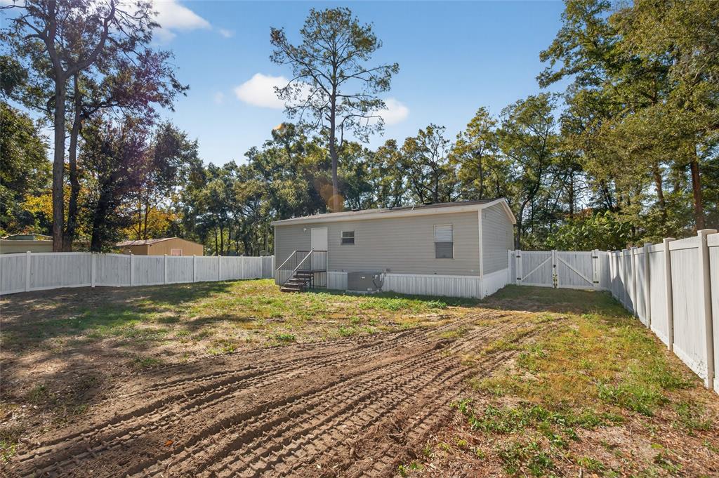 A single-story manufactured home sits in a fenced backyard with tire tracks on the ground — 3883 SE 55TH COURT, OCALA, FL