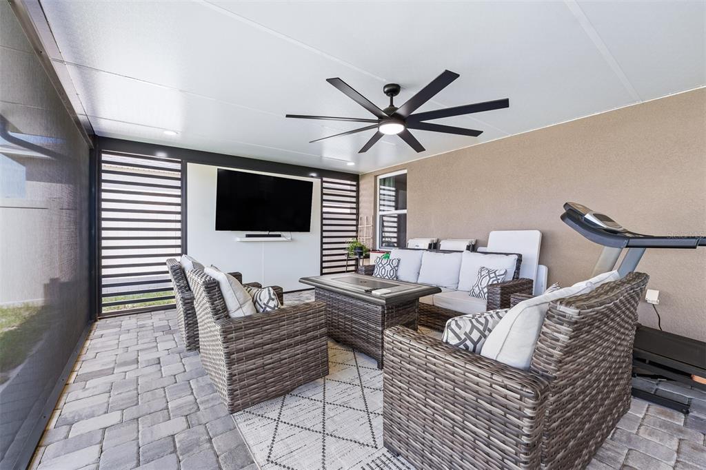 A covered outdoor patio features wicker furniture, a fire pit table, a television, and a treadmill — 4641 BERNARD BOULEVARD, HAINES CITY, FL