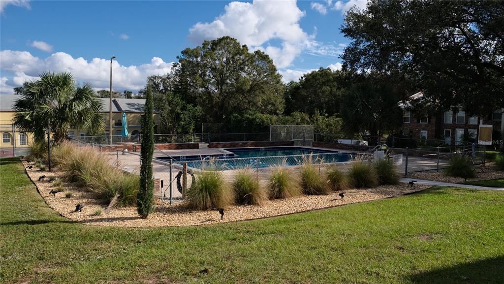 A fenced outdoor swimming pool is surrounded by landscaping and grass under a blue sky — 5850 CYPRESS GARDENS BOULEVARD UNIT 304, WINTER HAVEN, FL