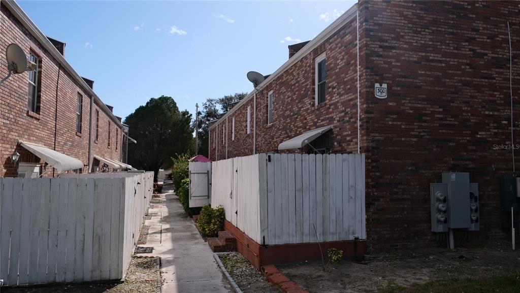 A narrow concrete walkway separates two rows of brick townhomes with white privacy fences — 5850 CYPRESS GARDENS BOULEVARD UNIT 304, WINTER HAVEN, FL