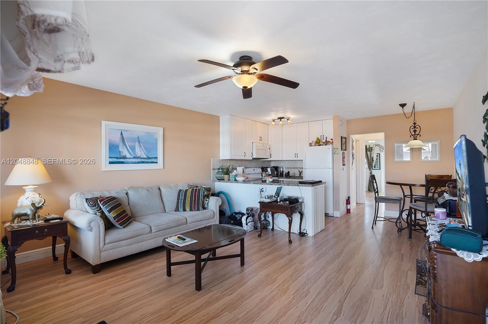 An open-concept living and dining area features light wood flooring, white cabinetry, and beige walls — 1000 SW 11 AVE # 17E, Hallandale Beach FL 33009, HALLANDALE BEACH, FL