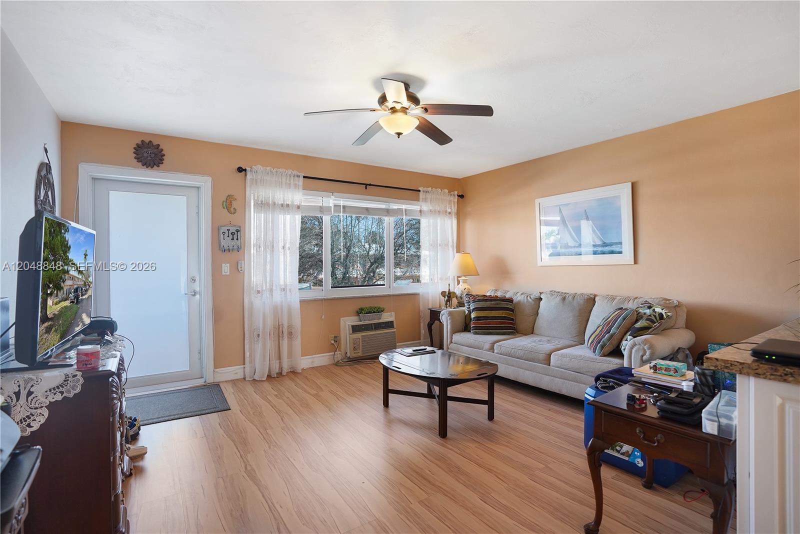 A living room features light wood flooring, peach-colored walls, a ceiling fan, and a sofa — 1000 SW 11 AVE # 17E, Hallandale Beach FL 33009, HALLANDALE BEACH, FL