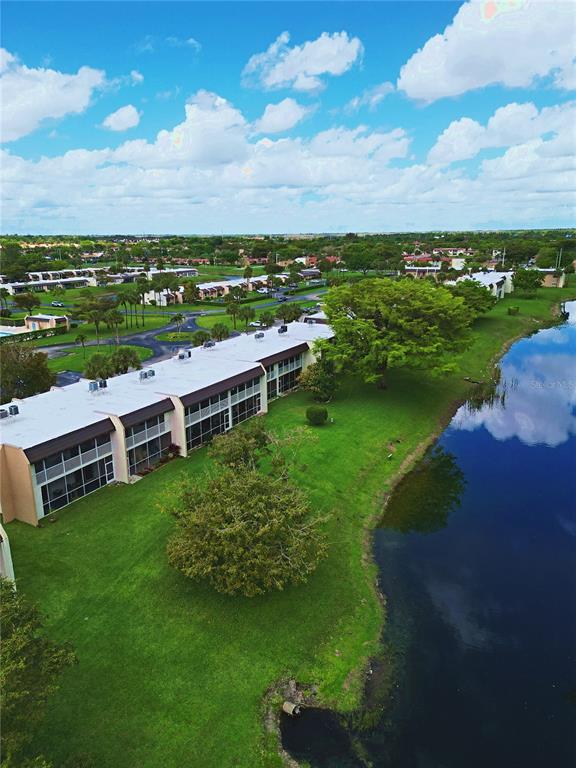 An aerial view shows a long, multi-story apartment building situated next to a large pond — 140 LAKE MERYL DRIVE UNIT 233, WEST PALM BEACH, FL