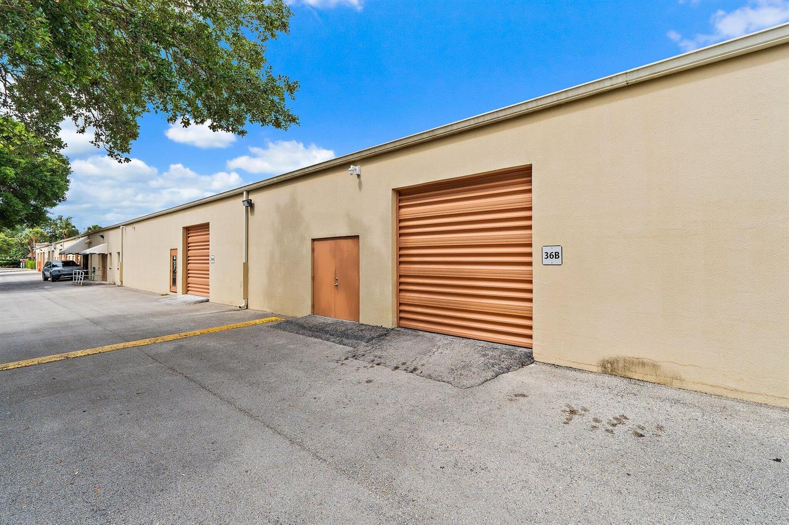 An exterior view of a commercial warehouse building with roll-up doors and a pedestrian entrance — 803 Maplewood Drive # 36b, Jupiter FL 33458, JUPITER, FL