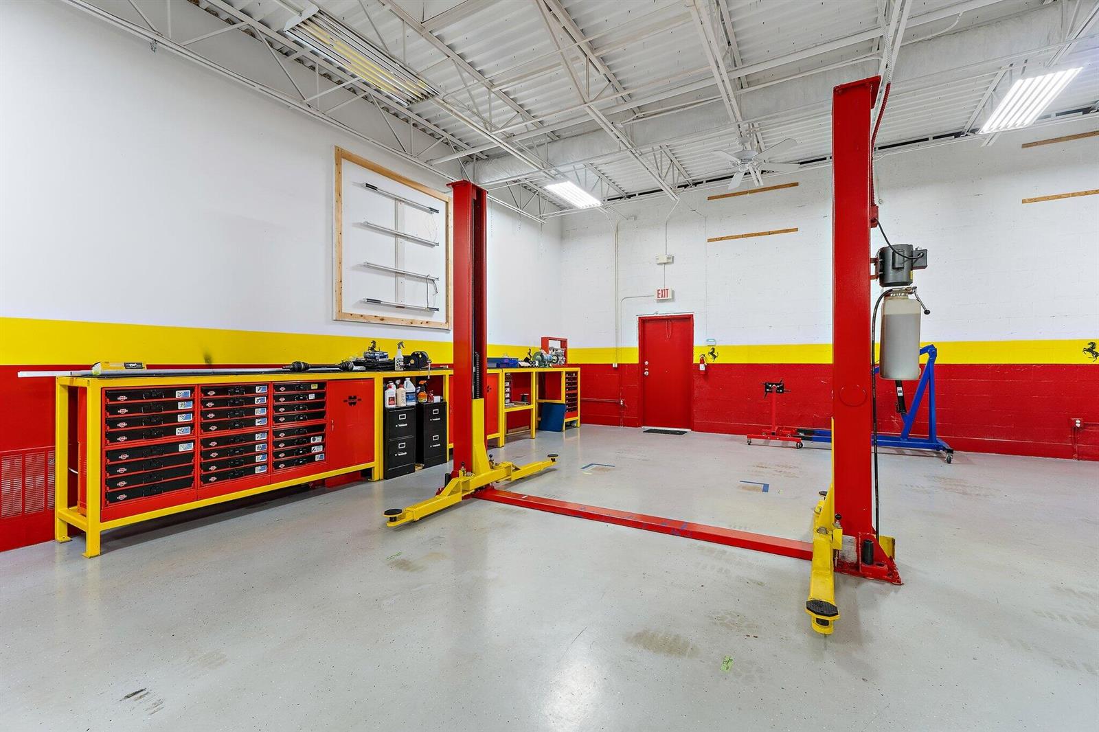A garage workspace features a two-post vehicle lift, red and yellow cabinets, and concrete floors — 803 Maplewood Drive # 36b, Jupiter FL 33458, JUPITER, FL