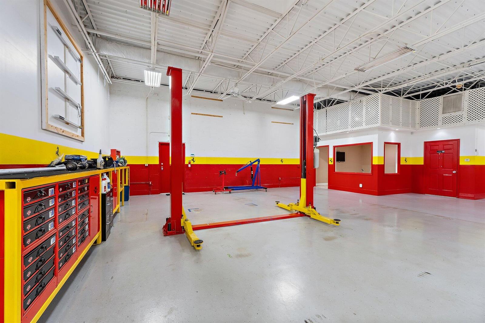 A garage workspace features a two-post car lift, red and yellow walls, and storage cabinets — 803 Maplewood Drive # 36b, Jupiter FL 33458, JUPITER, FL