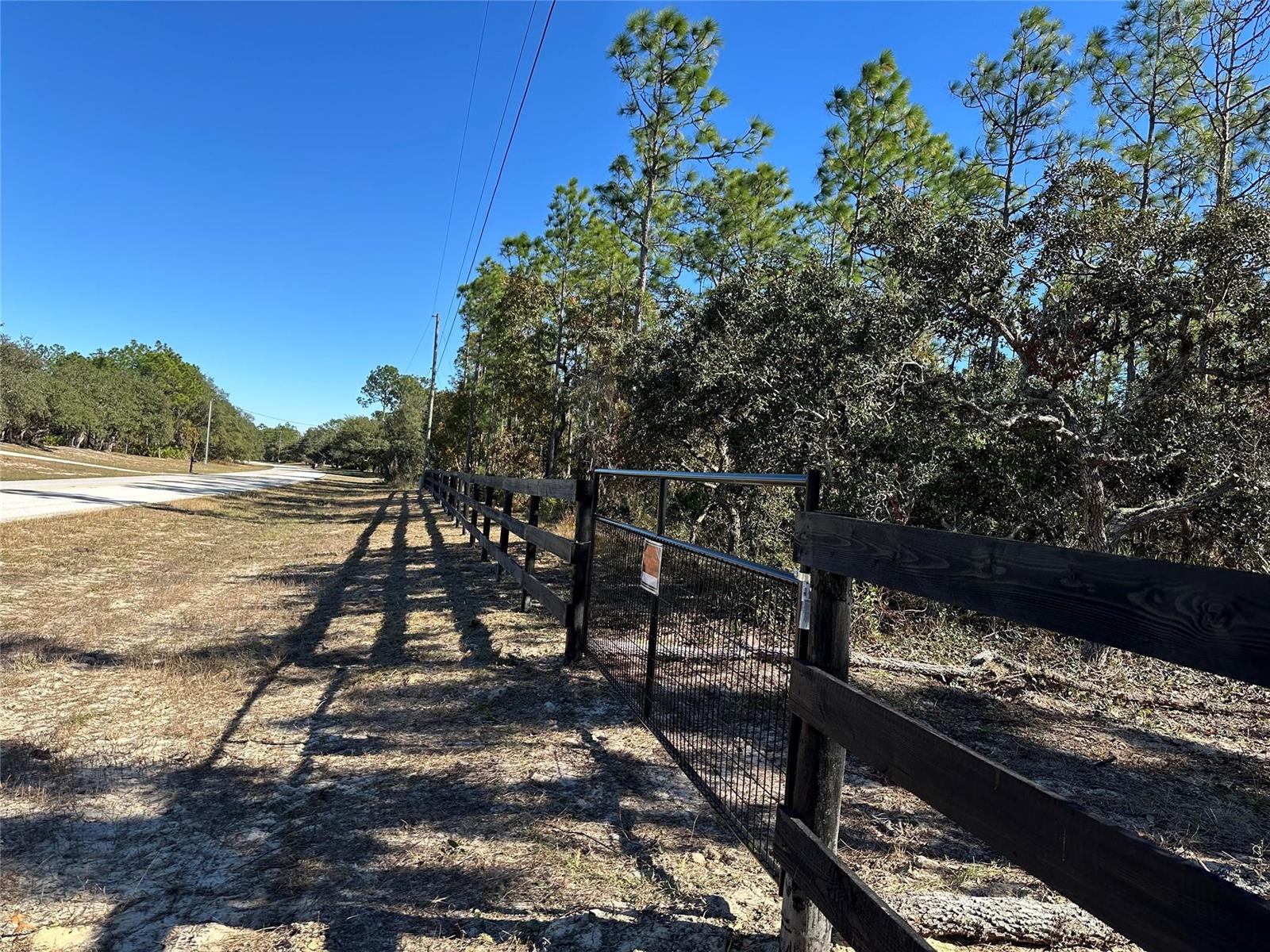 A black wooden fence with a wire gate runs along a sandy roadside — 4944 W Mustang Boulevard, FL 34465, FL