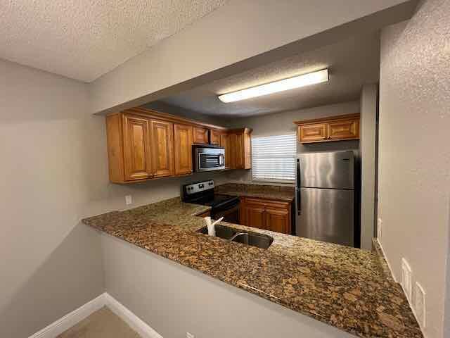 A kitchen with wood cabinets, granite countertops, and stainless steel appliances viewed over a counter — 1700 Windorah Way, West Palm Beach FL 33411, WEST PALM BEACH, FL