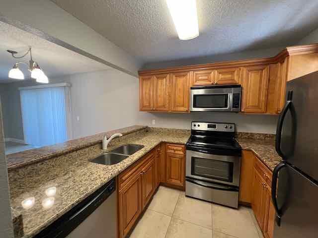 A kitchen with wood cabinets, granite countertops, stainless steel appliances, and tile flooring — 1700 Windorah Way, West Palm Beach FL 33411, WEST PALM BEACH, FL