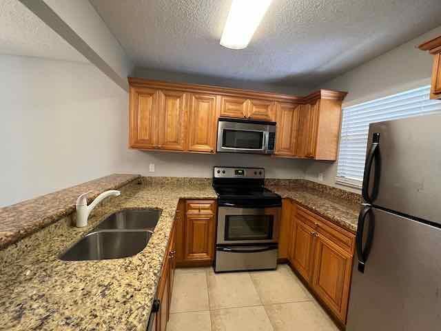 A kitchen features wooden cabinets, granite countertops, stainless steel appliances, and a double sink — 1700 Windorah Way, West Palm Beach FL 33411, WEST PALM BEACH, FL