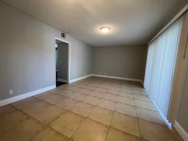 An empty room features light gray walls, tan tile flooring, and vertical window blinds — 1700 Windorah Way, West Palm Beach FL 33411, WEST PALM BEACH, FL