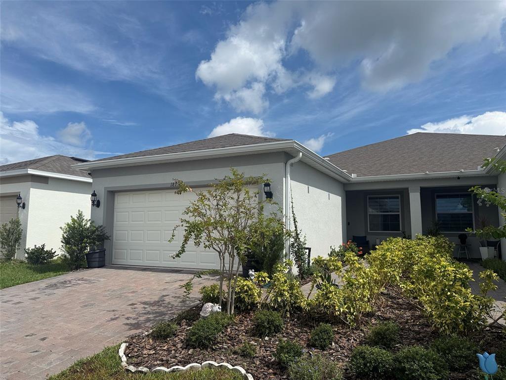 A single-story house with a white garage door, paved driveway, and landscaped front yard — 1873 SPRING SHOWER CIRCLE, KISSIMMEE, FL