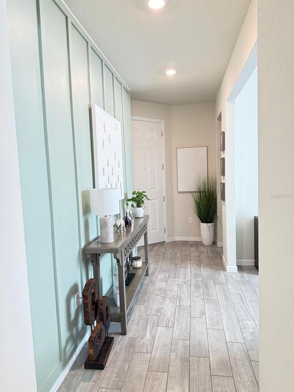 A hallway features light green board-and-batten wall paneling, a console table, and wood-look tile flooring — 1873 SPRING SHOWER CIRCLE, KISSIMMEE, FL