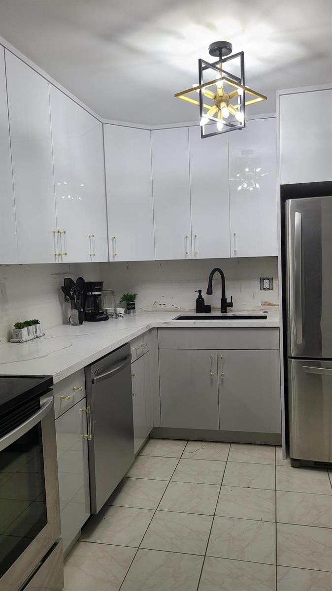 A kitchen features white upper cabinets, grey lower cabinets, stainless steel appliances, and a pendant light — 2500 Parkview Drive # 802, Hallandale Beach FL 33009, HALLANDALE BEACH, FL