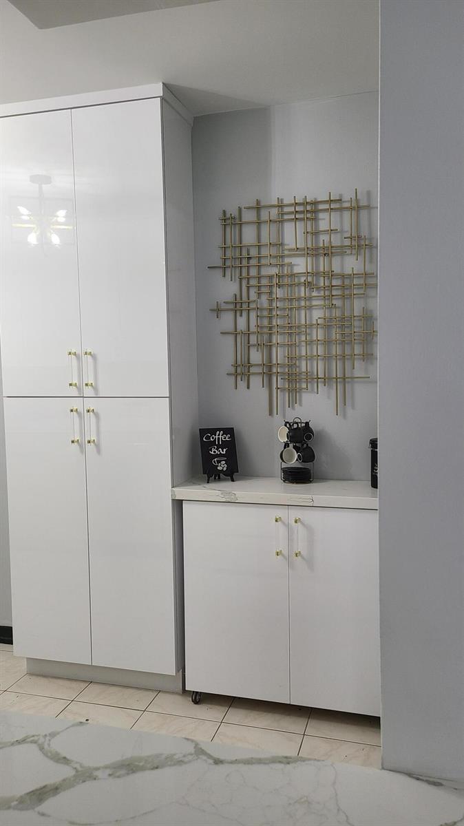 A white kitchen cabinet coffee bar features gold hardware and a geometric gold wall sculpture — 2500 Parkview Drive # 802, Hallandale Beach FL 33009, HALLANDALE BEACH, FL