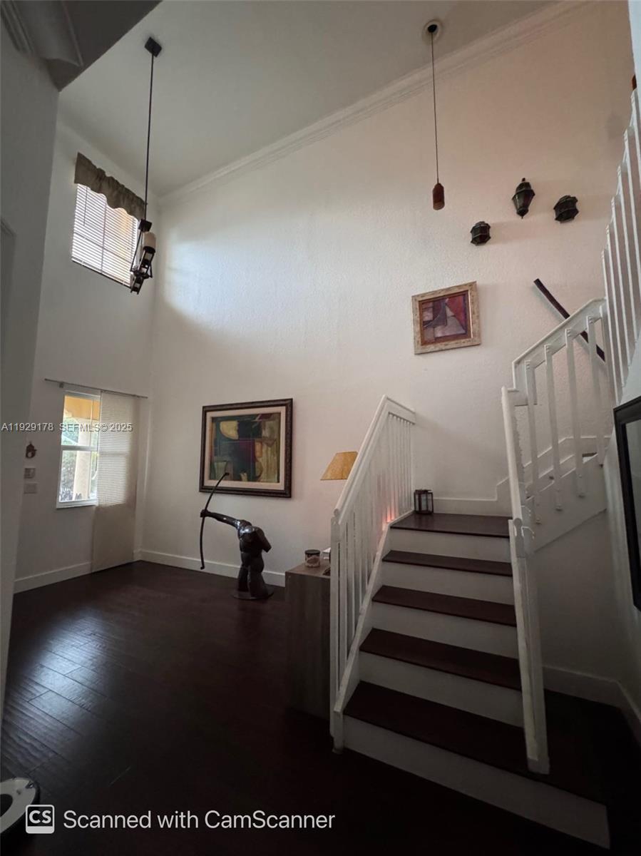 A high-ceilinged entryway features dark wood flooring, a white staircase, and decorative wall art — 15064 SW 8th Ln, Miami FL 33194, MIAMI, FL