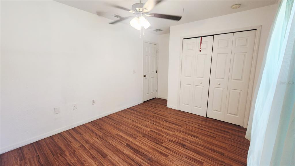 A bedroom features wood-look flooring, white walls, a ceiling fan, and a double-door closet — 11216 NW 8TH LANE, OCALA, FL