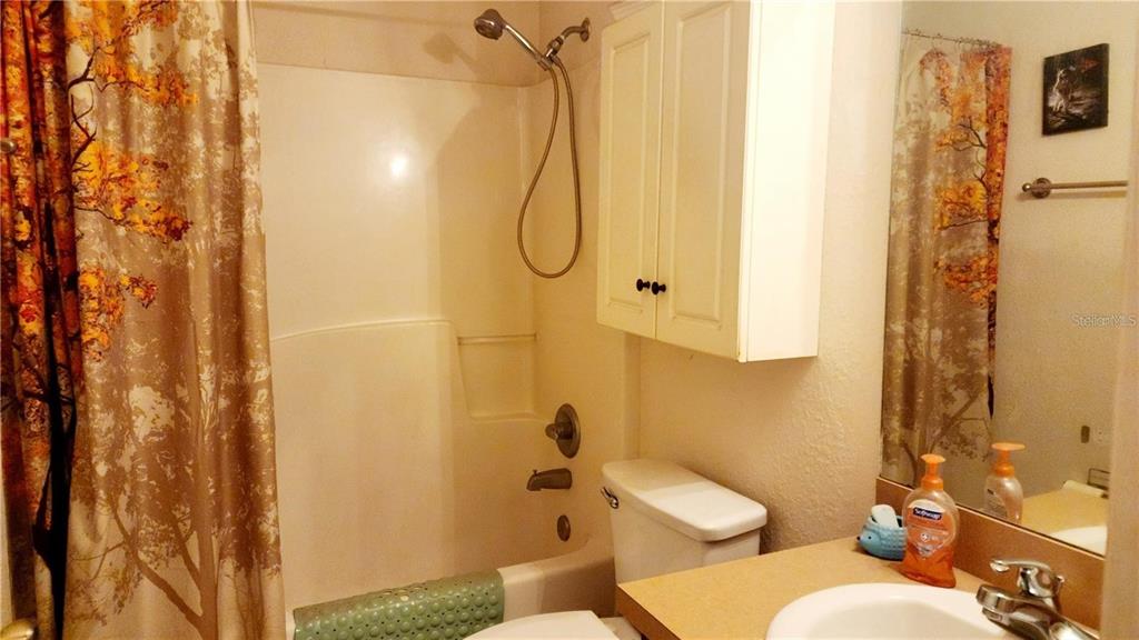 A bathroom features a shower-tub combination, a white vanity cabinet, and a beige countertop — 11216 NW 8TH LANE, OCALA, FL