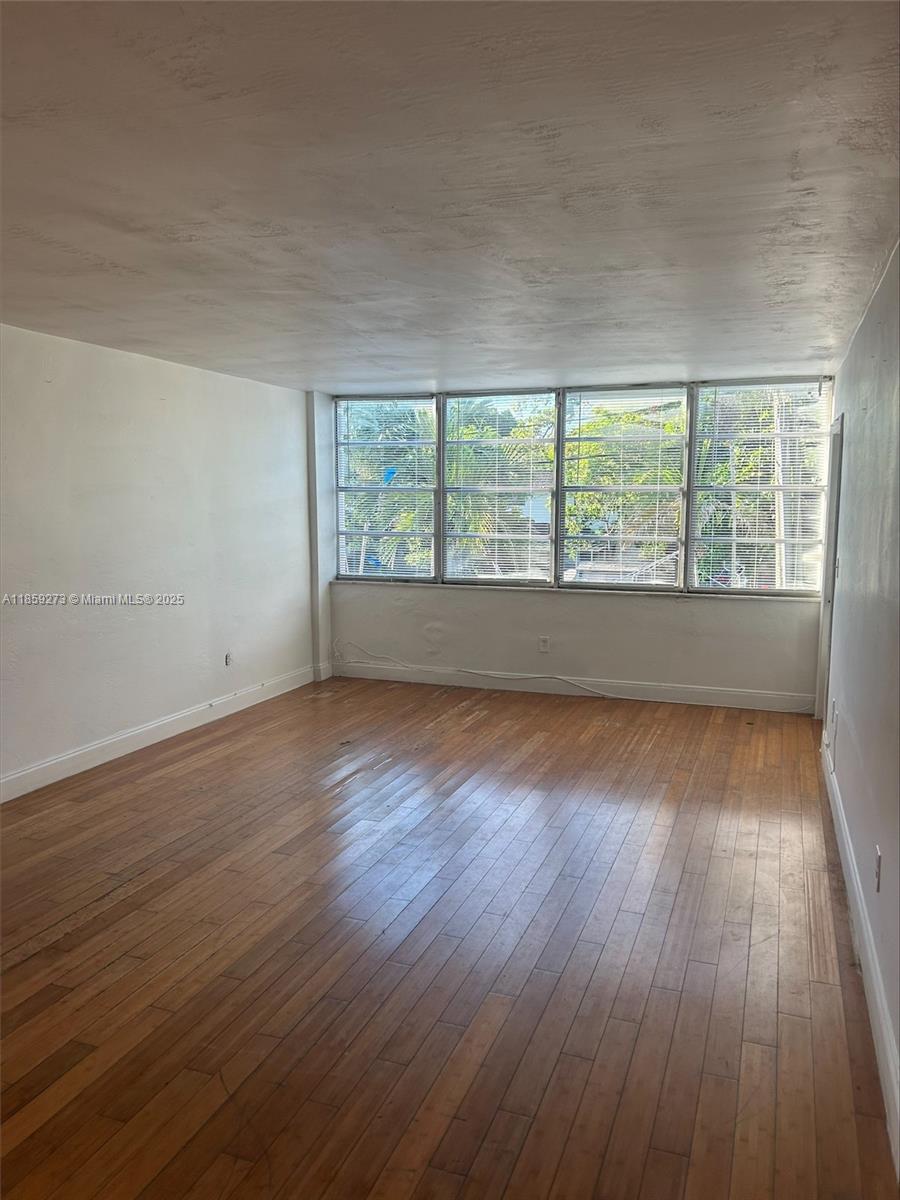 An empty room features hardwood flooring, white walls, and a large window with horizontal blinds — 2175 NE 170th St # 202, North Miami Beach FL 33162, NORTH MIAMI BEACH, FL