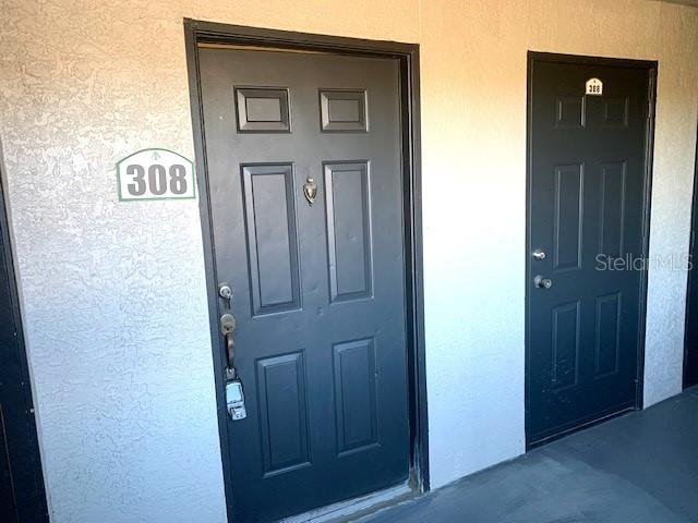 Two dark-colored apartment doors with unit numbers are set into a light-colored exterior wall — 8414 LUCUYA WAY UNIT 308, TEMPLE TERRACE, FL