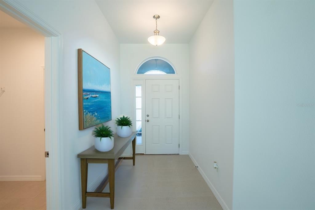 A bright entryway features a console table, two potted plants, and a white front door — 91 FLEMINGWOOD LANE, PALM COAST, FL