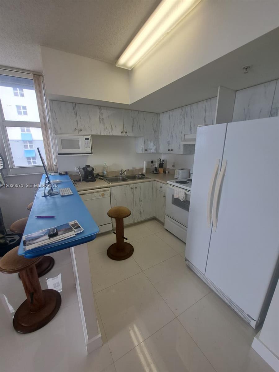 A kitchen features white marble-patterned cabinets, a blue breakfast bar, and white tile flooring — 5085 NW 7th St # 602, Miami FL 33126, MIAMI, FL