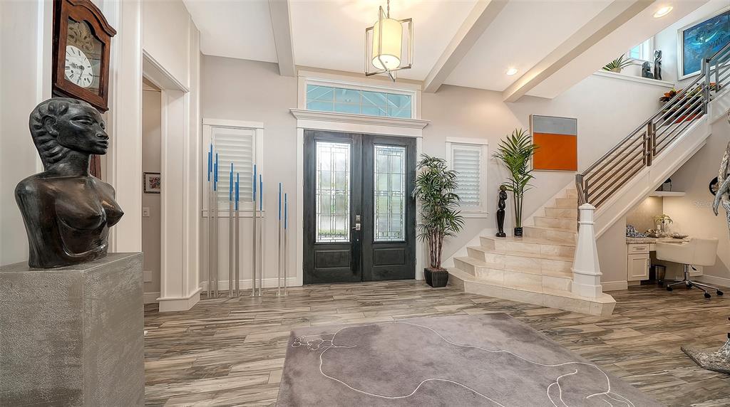 A grand foyer features a dark wood double door, a staircase, and modern art pieces — 1794 CUNLIFF LANE, SARASOTA, FL