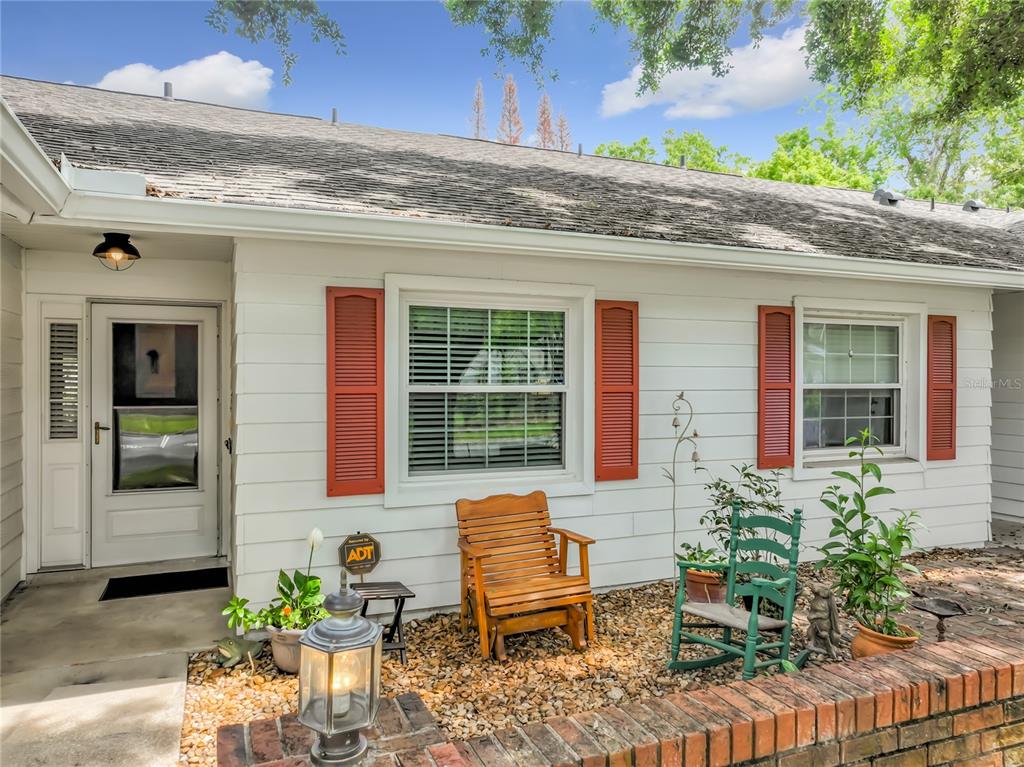 A white house exterior features red shutters, a front porch, and a brick wall — 5143 LAZY OAKS DRIVE UNIT 5143, WINTER PARK, FL