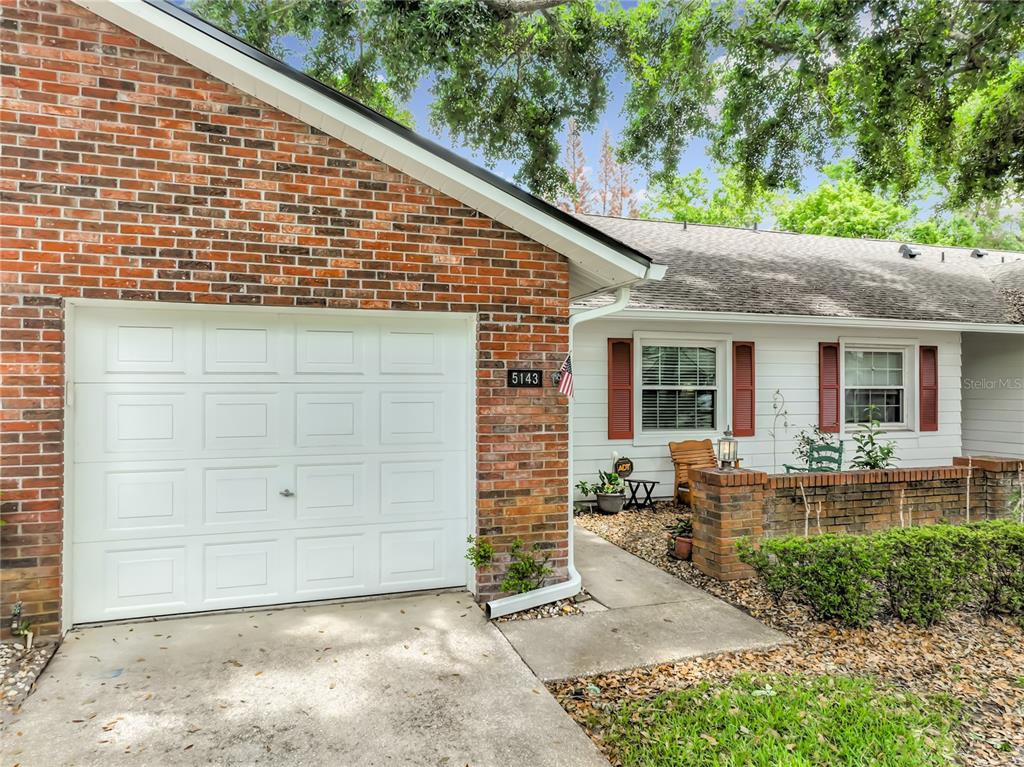 A brick and white siding house features a single-car garage and a front porch area — 5143 LAZY OAKS DRIVE UNIT 5143, WINTER PARK, FL