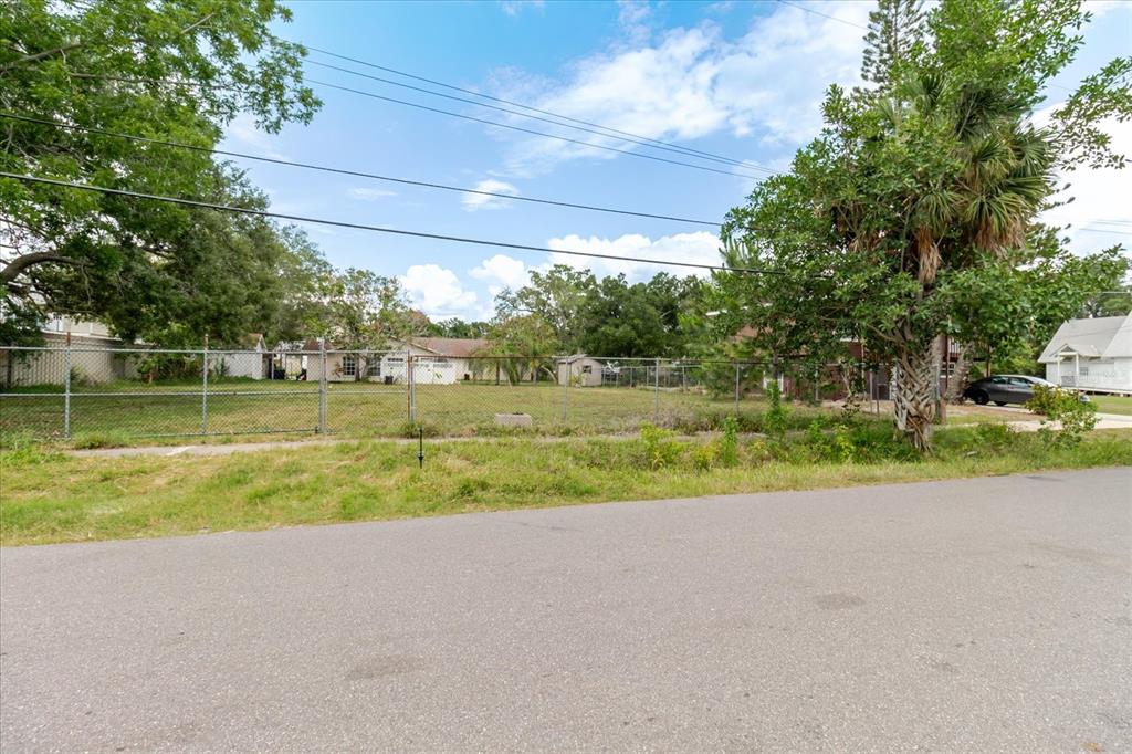 A fenced, vacant residential lot sits along a paved street under a blue sky — 7210 S SHERRILL STREET, TAMPA, FL