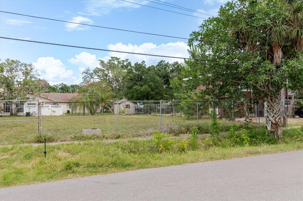 A fenced, grassy vacant lot sits beside a house under a blue sky — 7210 S SHERRILL STREET, TAMPA, FL