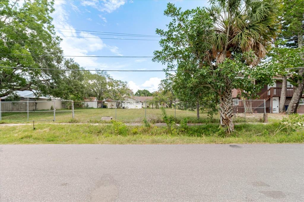 A vacant, fenced-in residential lot sits between two houses under a blue sky — 7210 S SHERRILL STREET, TAMPA, FL