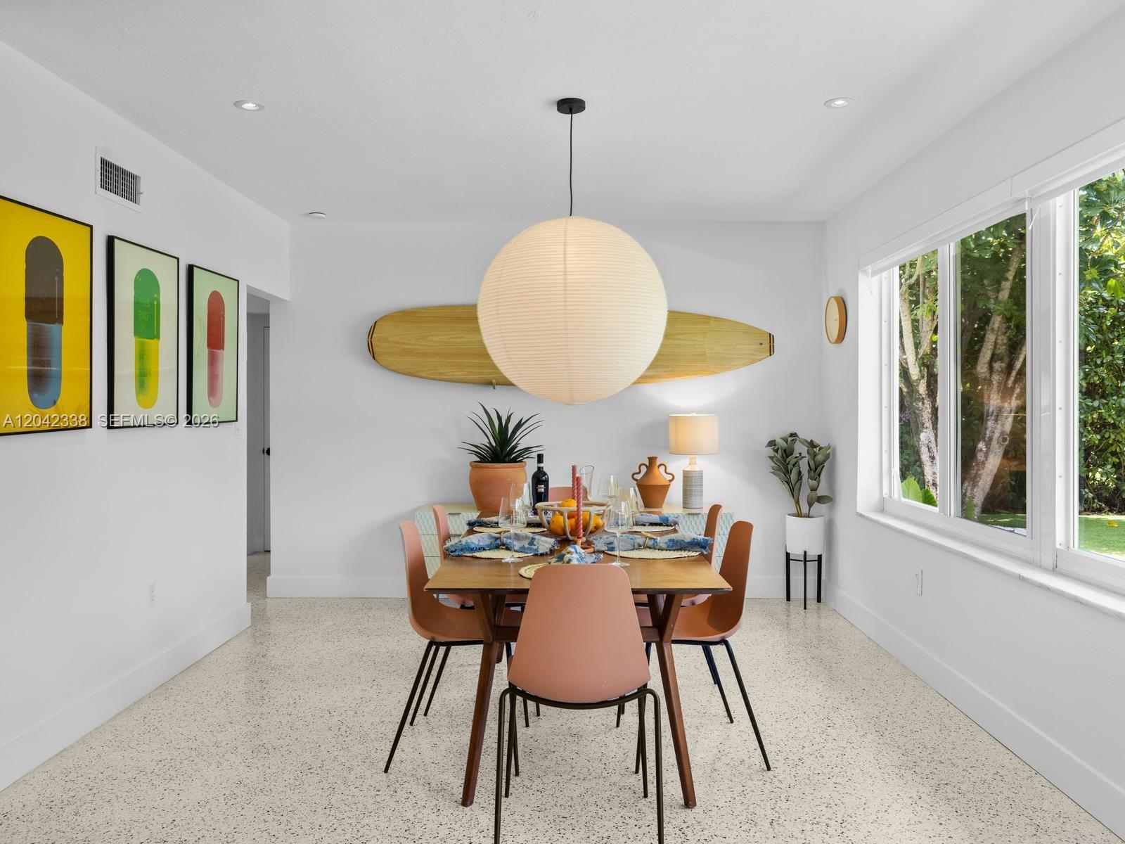 A dining room features a wooden table, mid-century chairs, a surfboard wall decoration, and terrazzo flooring — 1000 NE 85th St, Miami FL 33138, MIAMI, FL