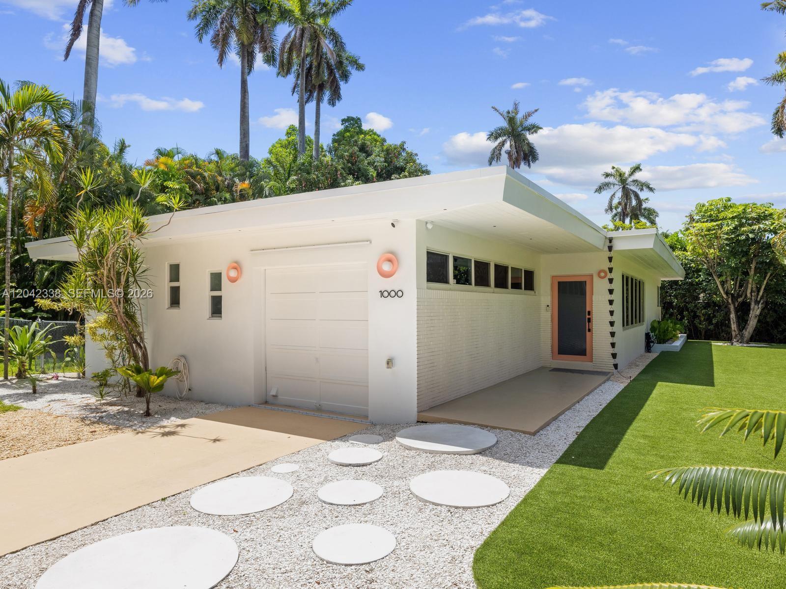 A white mid-century modern house features a garage, a pink door, and circular stepping stones — 1000 NE 85th St, Miami FL 33138, MIAMI, FL