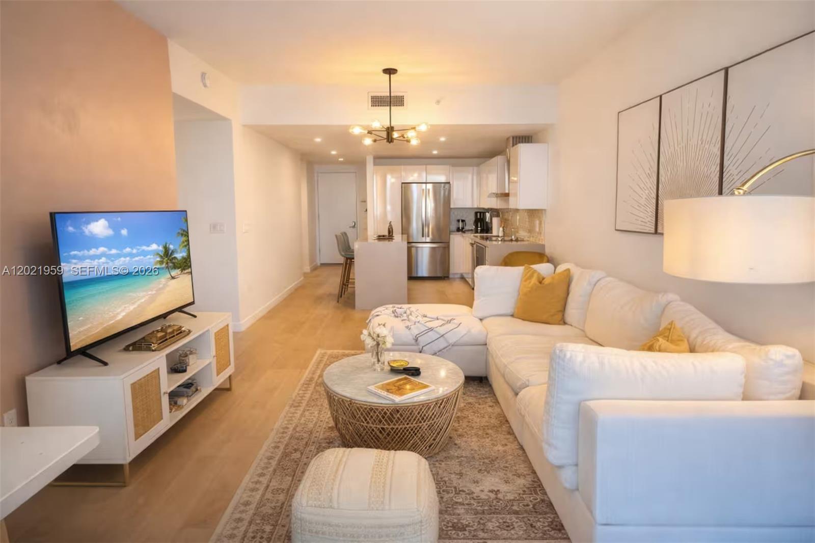 A living room with a white sectional sofa, coffee table, and television faces an open kitchen — 1600 NE 1st Ave # 1605, Miami FL 33132, MIAMI, FL